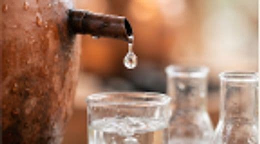 Clay distillation vessel dripping pure herbal essence into laboratory beakers